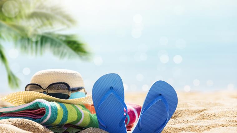 Staycation image of flip flops hat and sunglasses on a sandy beach