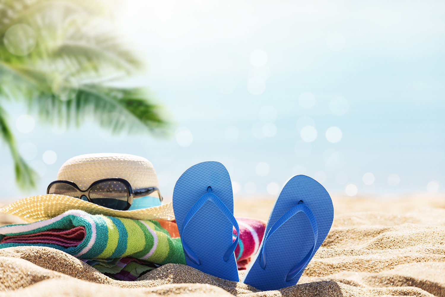 Staycation image of flip flops hat and sunglasses on a sandy beach
